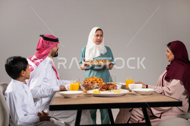 أجواء عائلية سعيدة، بورتريه لعاملة فلبينية تقوم بتحضير سفرة رمضان و وضع الطبق الرئيسي عليها, المقبلات و الاصناف العربية الشرقية, ايماءات السعادة بمناسبة قدوم الشهر الفضيل, الاحتفال بالاعياد و المناسبات الاسلامية, لمة الاهل على طاولة الطعام، خلفية رمادية
