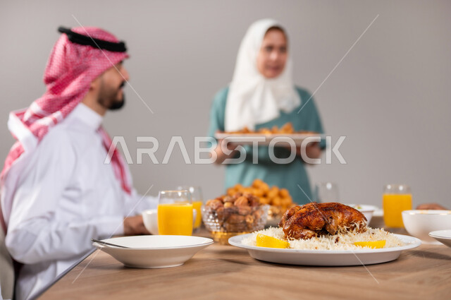 أجواء عائلية سعيدة، بورتريه لعاملة فلبينية تقوم بتحضير سفرة رمضان و وضع الطبق الرئيسي عليها, المقبلات و الاصناف العربية الشرقية, ايماءات السعادة بمناسبة قدوم الشهر الفضيل, الاحتفال بالاعياد و المناسبات الاسلامية, لمة الاهل على طاولة الطعام، خلفية رمادية