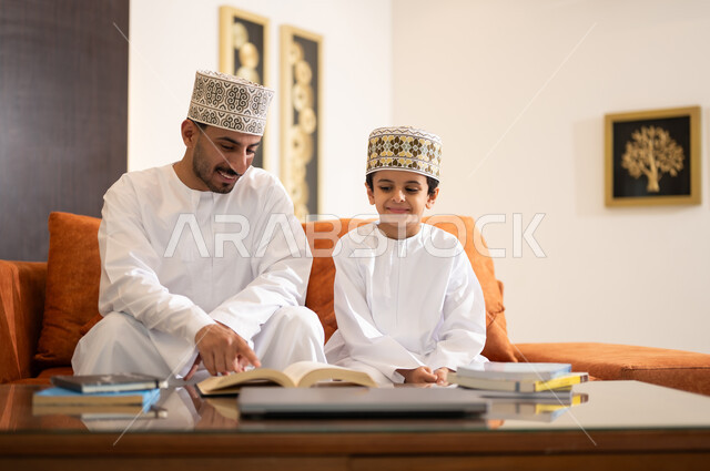 تنميه قدرات الاطفال بالتعلم، تشجيع وتطوير الاطفال بحل الواجبات المدرسيه المنزليه، بورتريه لأب عربي خليجي عماني يرتدي الدشداشه والكمه يقوم بمساعده ابنه في التعليم والقراءه، الانشطة التعليمية الالكترونيه  وانجاز الدروس والواجبات عن بعد باستخدام جهاز الايباد المحمول