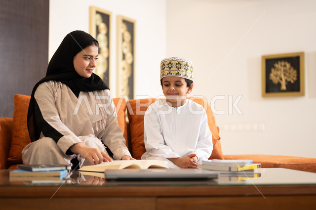 تنميه قدرات الاطفال بالتعلم، تشجيع وتطوير الاطفال بحل الواجبات المدرسيه المنزليه، بورتريه لأم عربية خليجية عمانيه محجبة تساعد طفلها في التعليم والقراءه، الانشطة التعليمية الالكترونيه  وانجاز الدروس والواجبات عن بعد باستخدام جهاز الايباد المحمول
