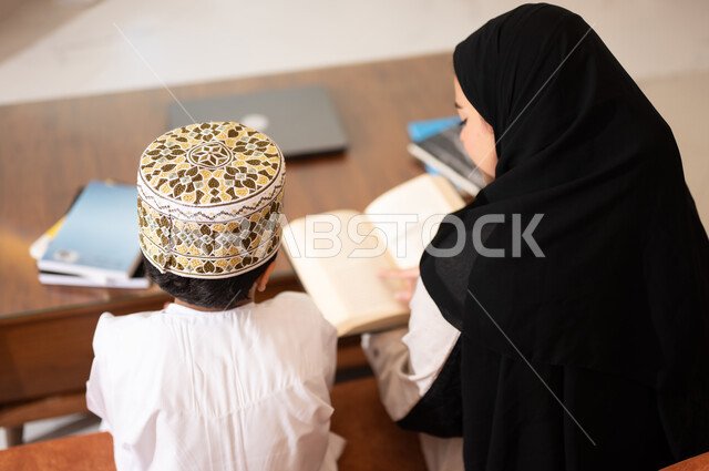 تنميه قدرات الاطفال بالتعلم، تشجيع وتطوير الاطفال بحل الواجبات المدرسيه المنزليه، بورتريه لأم عربية خليجية عمانيه محجبة تساعد طفلها في التعليم والقراءه، الانشطة التعليمية الالكترونيه  وانجاز الدروس والواجبات عن بعد باستخدام جهاز الايباد المحمول