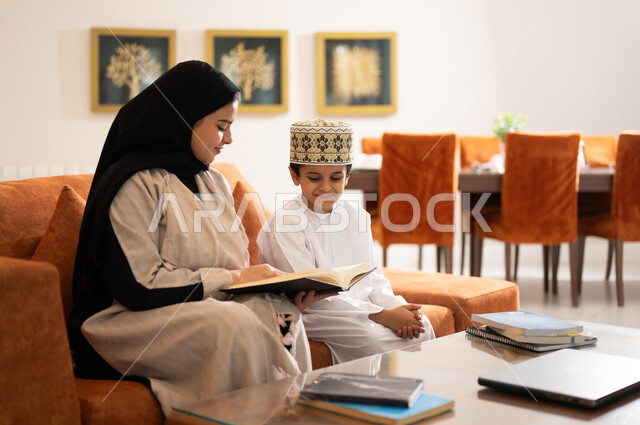 Developing children’s learning abilities, encouraging and developing children by solving home school assignments, a portrait of a veiled Arab, Gulf, Omani mother helping her child in education and reading, electronic educational activities, and completing lessons and assignments remotely using the portable iPad.