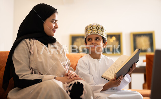 Developing children’s learning abilities, encouraging and developing children by solving home school assignments, a portrait of a veiled Arab, Gulf, Omani mother helping her child in education and reading, electronic educational activities, and completing lessons and assignments remotely using the portable iPad.