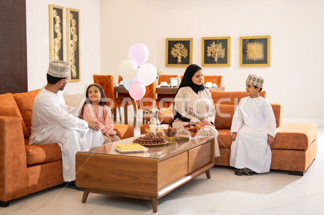 Family visits and the exchange of congratulations and greetings between family members with gestures of joy and happiness, the Eid atmosphere among the family, a portrait of an Arab Gulf-Omani family celebrating the Happy Eid, the provision of sweets and popular hospitality, holiday rituals and Islamic occasions in the Sultanate of Oman