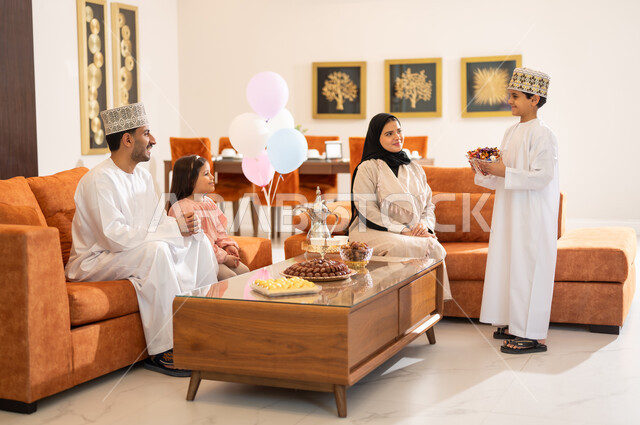 Family visits and the exchange of congratulations and greetings between family members with gestures of joy and happiness, the Eid atmosphere among the family, a portrait of an Arab Gulf-Omani family celebrating the Happy Eid, the provision of sweets and popular hospitality, holiday rituals and Islamic occasions in the Sultanate of Oman