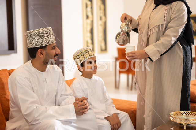 Popular Arab holiday hospitality in the Sultanate of Oman, family affection and love, a portrait of an Omani Gulf Arab family celebrating Islamic holidays, a veiled woman wearing the Omani abaya serving Gulf sweets and coffee, rituals of celebrations and happy occasions