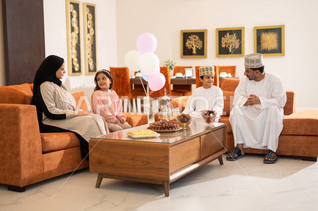 تجمع العائلة العمانية لاستقبال العيد المبارك, إظهار مشاعر الحنان والمحبة, الجلوس في غرفة المعيشة في جو عائلي دافئ، بورتريه لعائلة عربية خليجية عمانية تحتفل بالمناسبات الاسلامية برفقة بعضها البعض, ارتداء الثياب الجديدة الجميلة
