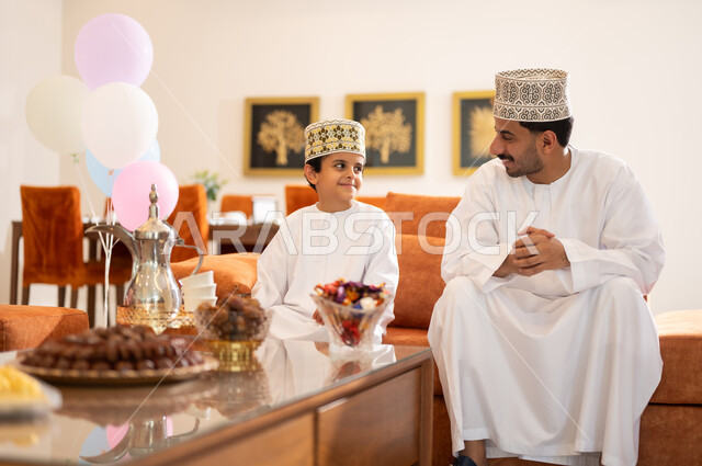 الزيارات العائلية وتبادل التهنئات والمعايدات بين أفراد الأسرة بإيماءات الفرح والسعادة, أجواء العيد بين الأهل, بورتريه لعائلة عربية خليجية عمانية تحتفل بالعيد السعيد, تقديم الحلويات والضيافة الشعبية, طقوس الأعياد والمناسبات الاسلامية في سلطنة عمان