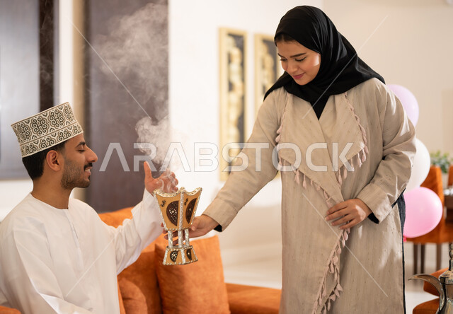 Celebration rituals on the morning of Eid, the family gathers and sits with each other, a portrait of a woman wearing the Omani abaya, fumigating and using luxurious oud perfumes to welcome the blessed Eid, an Omani Gulf Arab family celebrating Islamic occasions
