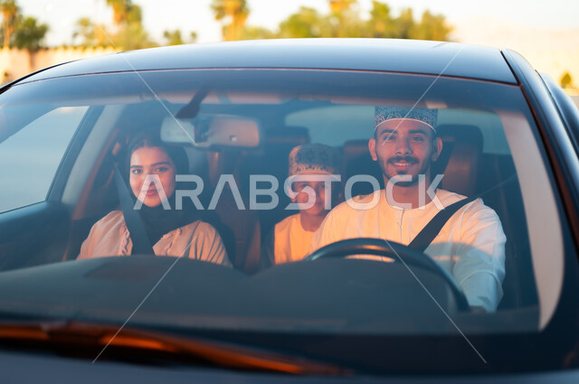 رحله جماعيه عائليه في السياره، دردشه ومحادثات في الطريق، التنزه في شوارع سلطنه عمان بورتريه لعائله عربيه خليجيه عمانيه مكونه من رجل وامرأه وصبي يرتديان الزي العماني التقليدي يجلسون داخل السياره ويلبسون احزمه الامان يقومون بجوله ترفيهيه، ايماءات تدل على السعاده والسرور وقضاء أوقات ممتعه