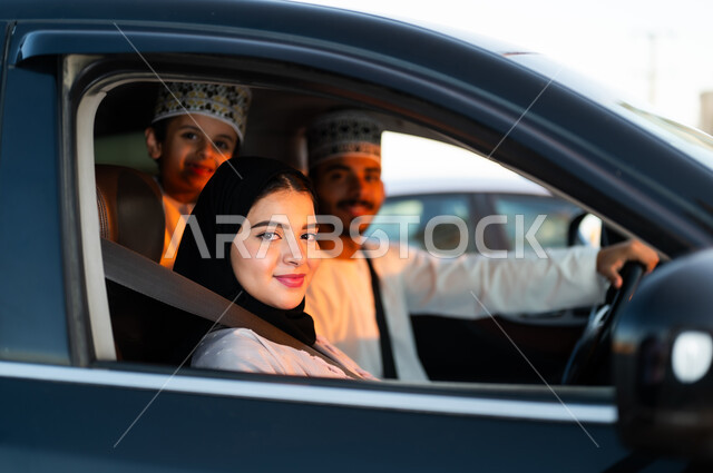 رحله جماعيه عائليه في السياره، دردشه ومحادثات في الطريق، التنزه في شوارع سلطنه عمان بورتريه لعائله عربيه خليجيه عمانيه مكونه من رجل وامرأه وصبي يرتديان الزي العماني التقليدي يجلسون داخل السياره ويلبسون احزمه الامان يقومون بجوله ترفيهيه، ايماءات تدل على السعاده والسرور وقضاء أوقات ممتعه
