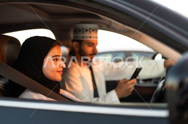 الاستمتاع للتنزه بالسياره  في شوارع سلطنه عمان، بورتريه لعائله خليجيه عربيه عمانيه يركبون السياره ويرتدون حزام الامان التزاما بقواعد السلامه المروريه ينظران الى الامام بابتسامه، الامساك بالهاتف الجوال والانشغال به اثناء القياده من مخاطر السلامه العامه