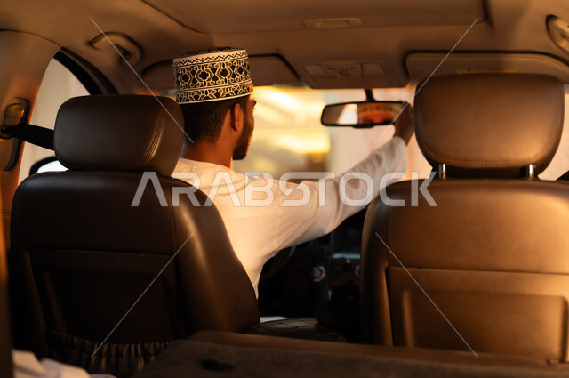 القياده بحذر واتباع قواعد السلامه، ركوب السياره والنظر الى الخلف , بورتريه لرجل عربي خليجي عماني يرتدي الدشداشه والكمه يجلس على كرسي القياده يقوم بتعديل المراه الاماميه للنظر الى ما ورائه، اهميه الاستعانه بالوسائل المساعده في السياره لتجنب الحوادث في الطرقات