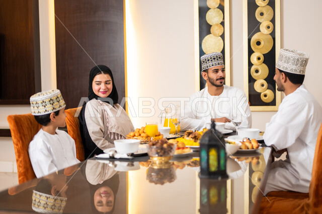 تجهيز وتحضير سفرة الإفطار، اجتماع الأسرة حول طاولة الطعام المليئه بأصناف المأكولات و المقبلات الشهية، ديكورات وأجواء رمضانية، بورتريه لعائله عربيه خليجيه عمانيه ترتدي الزي العماني التقليدي مجتمعين حول مائده الطعام في انتظار مدفع الافطار