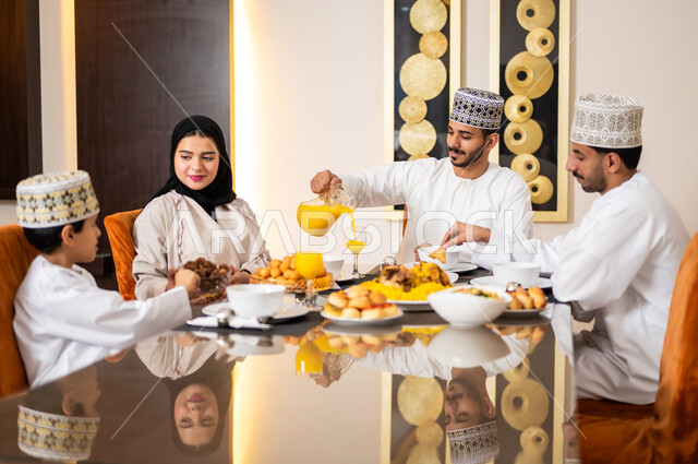 تجهيز وتحضير سفرة الإفطار، اجتماع الأسرة حول طاولة الطعام المليئه بأصناف المأكولات و المقبلات الشهية، ديكورات وأجواء رمضانية، بورتريه لعائله عربيه خليجيه عمانيه ترتدي الزي العماني التقليدي مجتمعين حول مائده الطعام في انتظار مدفع الافطار