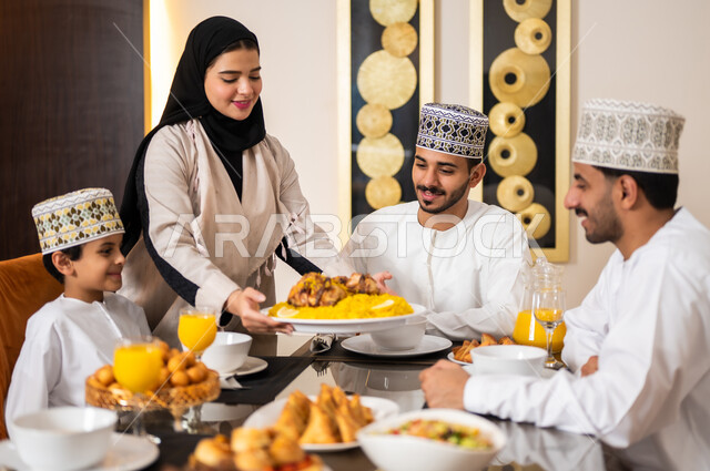 تجهيز وتحضير سفرة الإفطار، اجتماع الأسرة حول طاولة الطعام المليئه بأصناف المأكولات و المقبلات الشهية، ديكورات وأجواء رمضانية، بورتريه لعائله عربيه خليجيه عمانيه ترتدي الزي العماني التقليدي مجتمعين حول مائده الطعام في انتظار مدفع الافطار