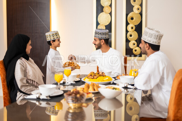 تجهيز وتحضير سفرة الإفطار، اجتماع الأسرة حول طاولة الطعام المليئه بأصناف المأكولات و المقبلات الشهية، ديكورات وأجواء رمضانية، بورتريه لعائله عربيه خليجيه عمانيه ترتدي الزي العماني التقليدي مجتمعين حول مائده الطعام في انتظار مدفع الافطار