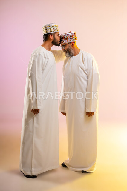 تقبيل رأس الأب والتهنئة بقدوم العيد، بورتريه لرجل عربي خليجي عماني يرتدي الدشداشة والكمه يقوم بمعايدة والده كبير السن في العيد، مشاعر الحب والمودة والأبوة، مفهوم بر الوالدين وتقديرهم، ارتداء الملابس العمانية التقليدية في الأعياد الإسلامية، خلفية ملونة