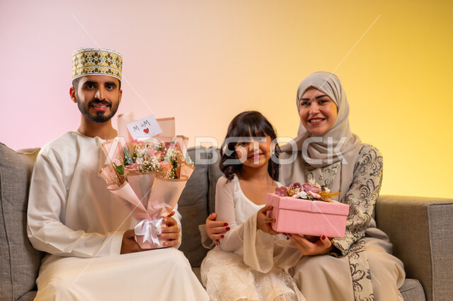 النظر للكاميرا بإيماءات الفرح والسرور، استقبال العيد بالهدايا والأزهار، تقدير الوالدين والبر بهم، المودة والمحبة بين أفراد الأسرة، بورتريه لرجل عربي خليجي عماني يرتدي الدشداشة والكمه يحمل باقة من الورود الملونة، عائلة عمانية تجلس وتحتفل بسعادة، بخلفية ملونة