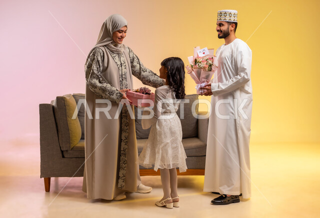 مفهوم تقدير الوالدين وإهداء الأم في العيد، المودة والمحبة بين أفراد الأسرة، تقوية الروابط الزوجية، بورتريه لرجل عربي خليجي عماني يرتدي الدشداشة والكمه يقوم بتقديم الورود لزوجته برفقه ابنته، عائلة عمانية تقوم بالاحتفال بقدوم العيد بإيماءات الفرح، خلفية ملونة