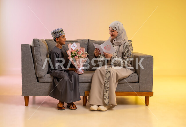 An atmosphere of family gathering on happy occasions and celebrations, Eid gifts and greeting cards, a portrait of an Arab Gulf Omani boy wearing a dishdasha and a cuff, giving his mother a bouquet of roses and a handwritten letter, the concept of gifting and appreciation to parents, an Omani family celebrating the blessed Eid, a colorful background