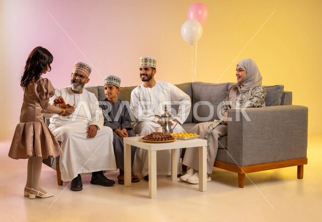 تقديم الحلويات والضيافة الشعبية, طقوس الأعياد والمناسبات الاسلامية في سلطنة عمان, الزيارات العائلية وتبادل التهنئات والمعايدات بين أفراد الأسرة بإيماءات الفرح والسعادة, أجواء العيد بين الأهل, بورتريه لعائلة عربية خليجية عمانية تحتفل بالعيد السعيد, خلفية ملونة