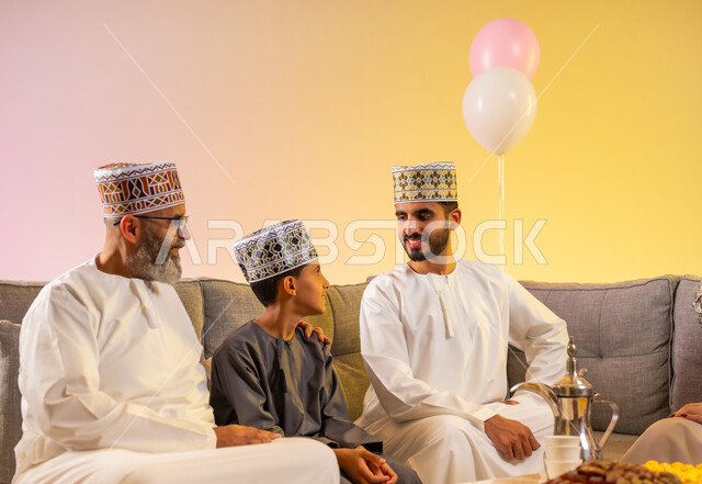 التهنئة والمعايدة بين أفراد الأسرة بإيماءات الفرح والسعادة, أجواء العيد بين الأهل, بورتريه لعائلة عربية خليجية عمانية تحتفل بالعيد السعيد, فتاة تقوم بتقديم الحلويات والضيافة الشعبية, طقوس الأعياد والمناسبات الاسلامية في سلطنة عمان, خلفية ملونة