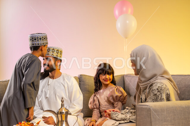 Kissing the father’s head with gestures of righteousness and satisfaction, gathering the family and sitting with each other happily, showing feelings of tenderness, love and affection, wearing traditional Omani clothes to welcome the blessed Eid, portrait of an Arab Gulf Omani family celebrating Islamic occasions, colorful background.