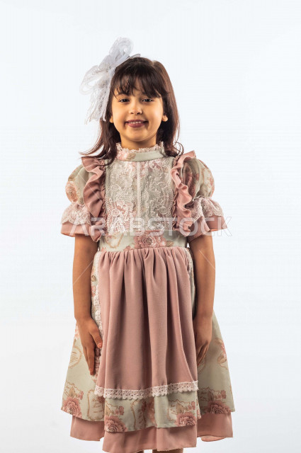 خلفية بيضاء لفتاه صغيرة سعودية خليجية مبتسمة وجميلة ، تنظر الى الكاميرا بإيماءات وجه ويدين مختلفة , بورتريه لطفلة سعودية خليجية سعيدة ترتدي لباس العيد الانيق , الاحتفال بعيد الفطر السعيد ، عيد الفطر المبارك