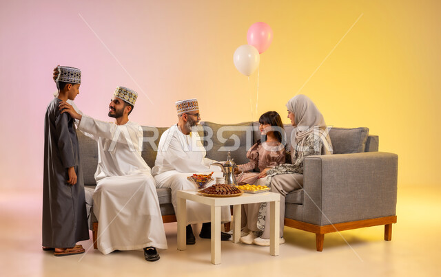 ارتداء الثياب العمانية التقليدية, تجمع العائلة لاستقبال العيد المبارك, إظهار مشاعر الحنان والمحبة والمودة, الجلوس في غرفة المعيشة في جو عائلي دافئ، بورتريه لعائلة عربية خليجية عمانية تحتفل بالمناسبات الاسلامية برفقة بعضها البعض, خلفية ملونة