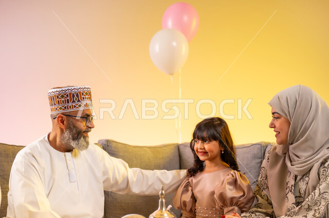 Rejoicing at the arrival of the blessed Eid, sitting in the living room in a warm family atmosphere, a portrait of an Arab Gulf Omani family celebrating Islamic occasions in the company of each other, the grandfather and his granddaughter gathering and showing feelings of tenderness and love, wearing beautiful new clothes, a colorful background