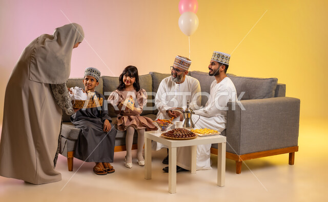 مفهوم المحبة والمودة بين أفراد الأسرة، تقديم الضيافة العربية والحلويات الشعبية، التهنئات وطقوس المناسبات الاسلامية، الزيارات والجلوس في غرفة المعيشة في جو عائلي، بورتريه لعائلة عربية خليجية عمانية ترتدي الأزياء التقليدية تحتفل بقدوم العيد, خلفية ملونة