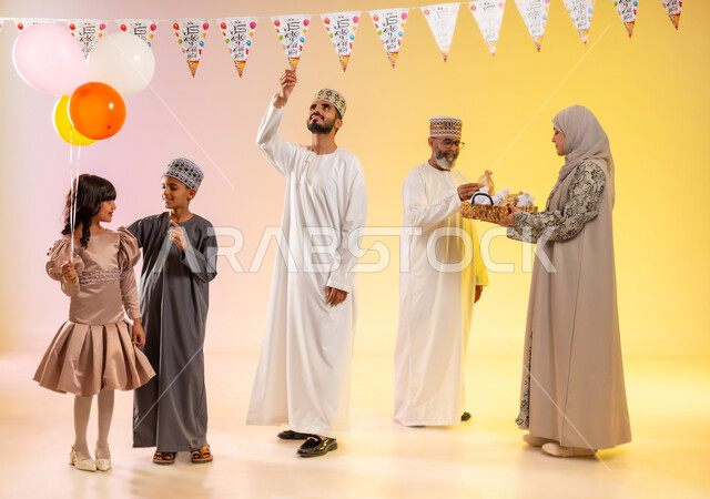 تعليق حبال الزينة المبهجة، طقوس الاحتفالات والمناسبات السعيدة في سلطنة عمان، تقديم الضيافة وتوزيع الحلويات الشعبية في العيد، بورتريه لعائلة عربية خليجية عمانية تظهر مشاعر الفرح والسعادة بالاحتفال بالأعياد، الوقوف وارتداء الأزياء العمانية التقليدية، خلفية ملونة