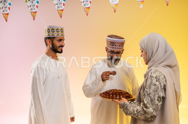 جو البهجة والفرح والزينة، طقوس الاحتفالات والمناسبات السعيدة في سلطنة عمان، توزيع الحلويات الشعبية في الأعياد، بورتريه مقرب لعائلة عربية خليجية عمانية تحتفل بالعيد المبارك، ارتداء الأزياء العمانية التقليدية، مفهوم الكرم وتقديم الضيافة العربية، خلفية ملونة