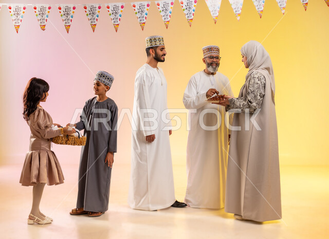 توزيع الحلويات الشعبية وتقديم الضيافة في العيد، بورتريه لعائلة عربية خليجية عمانية تظهر مشاعر الفرح والسعادة بالاحتفال بالأعياد، الوقوف وارتداء الأزياء العمانية التقليدية، طقوس الاحتفالات والمناسبات السعيدة في سلطنة عمان، تعليق حبال الزينة المبهجة، خلفية ملونة