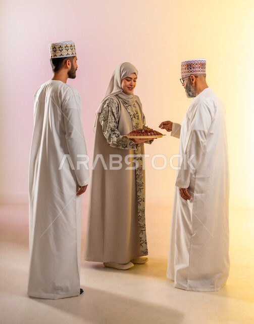 Family affection and love, a portrait of an Omani Gulf Arab family celebrating Islamic holidays, a veiled woman wearing an abaya serving traditional sweets, rituals of celebrations and happy occasions, popular Arab holiday hospitality in the Sultanate of Oman, a colorful background