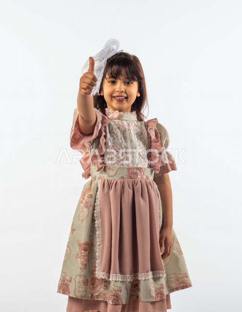 خلفية بيضاء لفتاه صغيرة سعودية خليجية مبتسمة وجميلة ، تنظر الى الكاميرا بإيماءات وجه ويدين مختلفة , بورتريه لطفلة سعودية خليجية سعيدة ترتدي لباس العيد الانيق , الاحتفال بعيد الفطر السعيد ، عيد الفطر المبارك