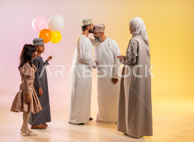 السلام وتقبيل رأس الجد والتهنئة بقدوم العيد, البلالين الملونة والزينة، إظهار مشاعر المودة والمحبة العائلية, أجواء البهجة والسعادة والاحتفال, بورتريه لعائلة عربية خليجية عمانية تحتفل بالأعياد الاسلامية, تقديم الحلويات التقليدية والمأكولات الشهية, خلفية ملونة