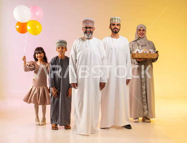 الوقوف والنظر للكاميرا بإيماءات السعادة والفرح، طقوس الاحتفالات بالعيد وارتداء الثياب الجديدة, بورتريه لعائلة عربية خليجية عمانية تحتفل بالأعياد الاسلامية, تقديم الحلويات التقليدية والمأكولات الشهية, إظهار مشاعر المودة والمحبة العائلية, خلفية ملونة