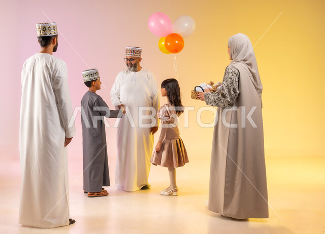 البلالين الملونة والزينة، إظهار مشاعر المودة والمحبة العائلية, أجواء البهجة والسعادة في العيد, بورتريه لعائلة عربية خليجية عمانية تحتفل بالأعياد الاسلامية, التحية والمصافحة بين أفراد الأسرة و التهنئات, تقديم الحلويات التقليدية والمأكولات الشهية, خلفية ملونة