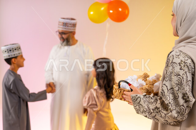 أجواء البهجة والسعادة في العيد, بورتريه لعائلة عربية خليجية عمانية تحتفل بالأعياد الاسلامية, التحية والمصافحة بين أفراد الأسرة و التهنئات, البلالين الملونة والزينة، تقديم الحلويات التقليدية والمأكولات الشهية, إظهار مشاعر المودة والمحبة العائلية, خلفية ملونة