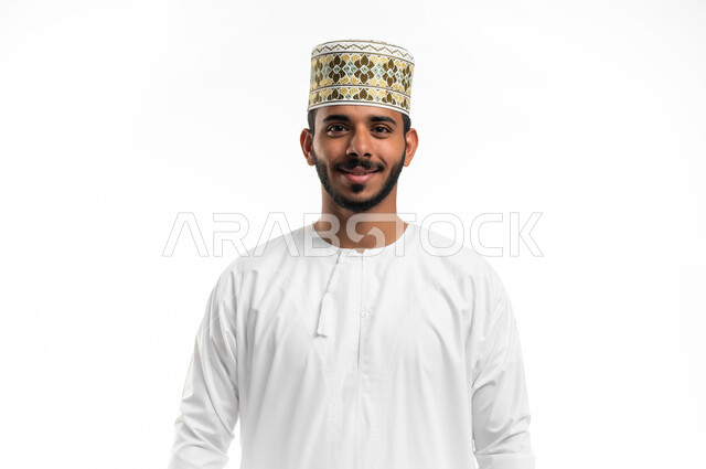 مفهوم الرجولة والثقة بالنفس، التقاط الصور الشخصية للوثائق الرسمية، بورتريه مقرب لشاب عربي خليجي عماني مبتسم يرتدي الدشداشة و الكمه ينظر الى الكاميرا بإيماءات السرور والسعادة، الاهتمام بالأناقة والمظهر الخارجي، خلفية بيضاء