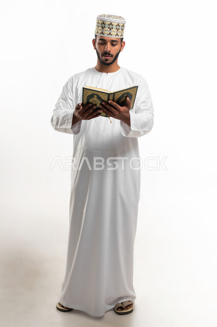 الاجتهاد في العبادة، تلاوة وقراءة القرآن الكريم وتدبر معانيه، بورتريه لشاب عربي خليجي عماني يرتدي الدشداشة والكمه يحمل بيده المصحف الشريف، الإكثار من ذكر الله تعالى، التقرب الى الله في شهر رمضان، الشعور بالخشوع والطمأنينة، الطول الكامل للجسم, خلفية بيضاء