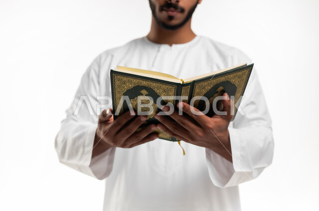 الشعور بالخشوع والطمأنينة، الاجتهاد في العبادة، تلاوة وقراءة القرآن الكريم وتدبر معانيه، بورتريه مقرب لشاب عربي خليجي عماني يرتدي الدشداشة والكمه يحمل بيده المصحف الشريف، الإكثار من ذكر الله تعالى، التقرب الى الله في شهر رمضان، خلفية بيضاء