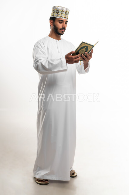 الاجتهاد في العبادة، تلاوة وقراءة القرآن الكريم وتدبر معانيه، بورتريه لشاب عربي خليجي عماني يرتدي الدشداشة والكمه يحمل بيده المصحف الشريف، الإكثار من ذكر الله تعالى، التقرب الى الله في شهر رمضان، الشعور بالخشوع والطمأنينة، الطول الكامل للجسم, خلفية بيضاء