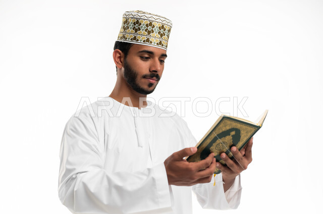 الشعور بالخشوع والطمأنينة، الاجتهاد في العبادة، تلاوة وقراءة القرآن الكريم وتدبر معانيه، بورتريه مقرب لشاب عربي خليجي عماني يرتدي الدشداشة والكمه يحمل بيده المصحف الشريف، الإكثار من ذكر الله تعالى، التقرب الى الله في شهر رمضان،  خلفية بيضاء