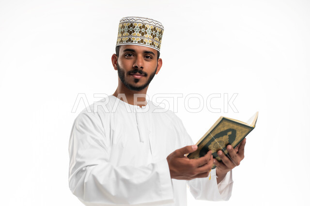 تلاوة وقراءة القرآن الكريم وتدبر معانيه، بورتريه مقرب لشاب عربي خليجي عماني يرتدي الدشداشة والكمه ينظر الى الكاميرا ويحمل بيده المصحف الشريف، الإكثار من ذكر الله تعالى، الاجتهاد في العبادة، التقرب الى الله في شهر رمضان، الشعور بالخشوع والطمأنينة، خلفية بيضاء