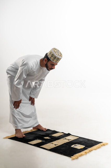 الحفاظ على إقامة الصلوات الخمس بوقتها، أهمية الالتزام بالصلاة على وقتها، التقرب من الله تعالى بأداء الفرائض والتزام أوامره, الركن الثاني من اركان الاسلام، بورتريه لشاب عربي خليجي عماني يرتدي الدشداشة والكمه يركع لله تعالى، خلفية بيضاء