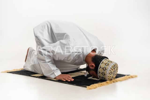 أهمية الالتزام بالصلاة على وقتها، التقرب من الله تعالى بأداء الفرائض والتزام أوامره, الركن الثاني من اركان الاسلام، بورتريه لشاب عربي خليجي عماني يرتدي الدشداشة والكمه يسجد لله تعالى،  الحفاظ على إقامة الصلوات الخمس بوقتها، خلفية بيضاء