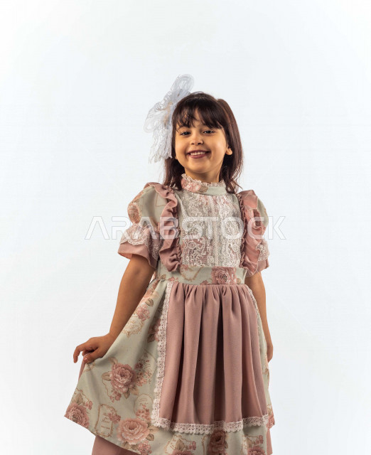 خلفية بيضاء لفتاه صغيرة سعودية خليجية مبتسمة وجميلة ، تنظر الى الكاميرا بإيماءات وجه ويدين مختلفة , بورتريه لطفلة سعودية خليجية سعيدة ترتدي لباس العيد الانيق , الاحتفال بعيد الفطر السعيد ، عيد الفطر المبارك